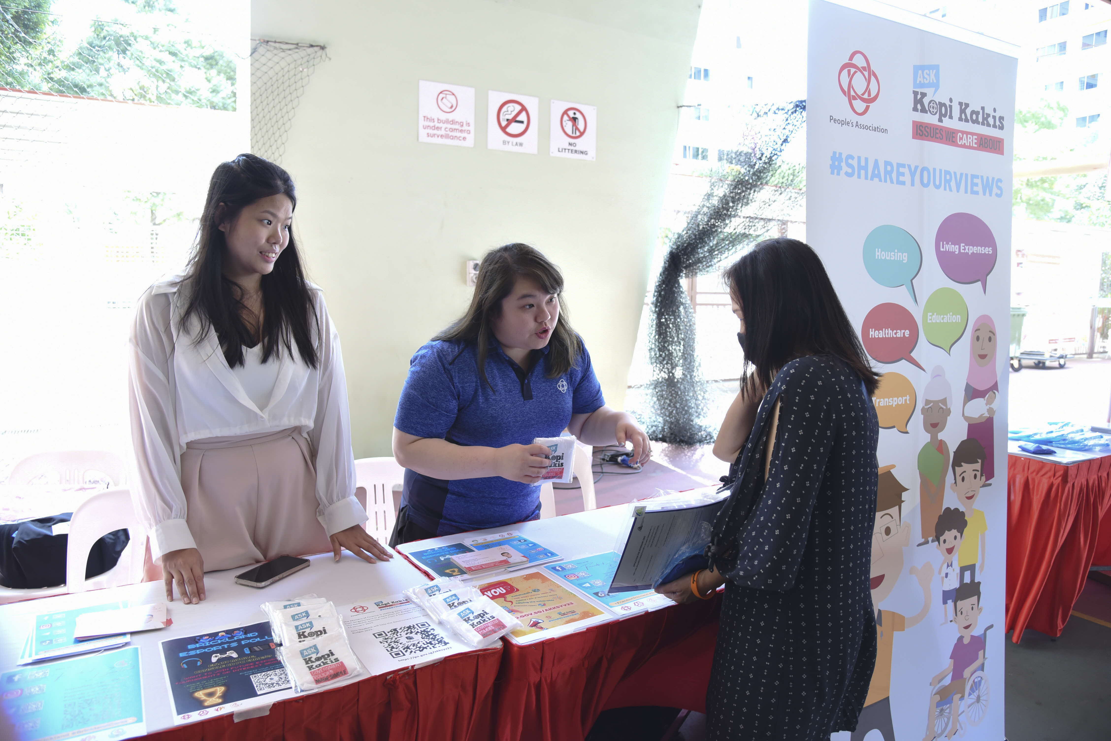 People at a booth with pamphlets and a sign about community issues like housing, healthcare, and education.